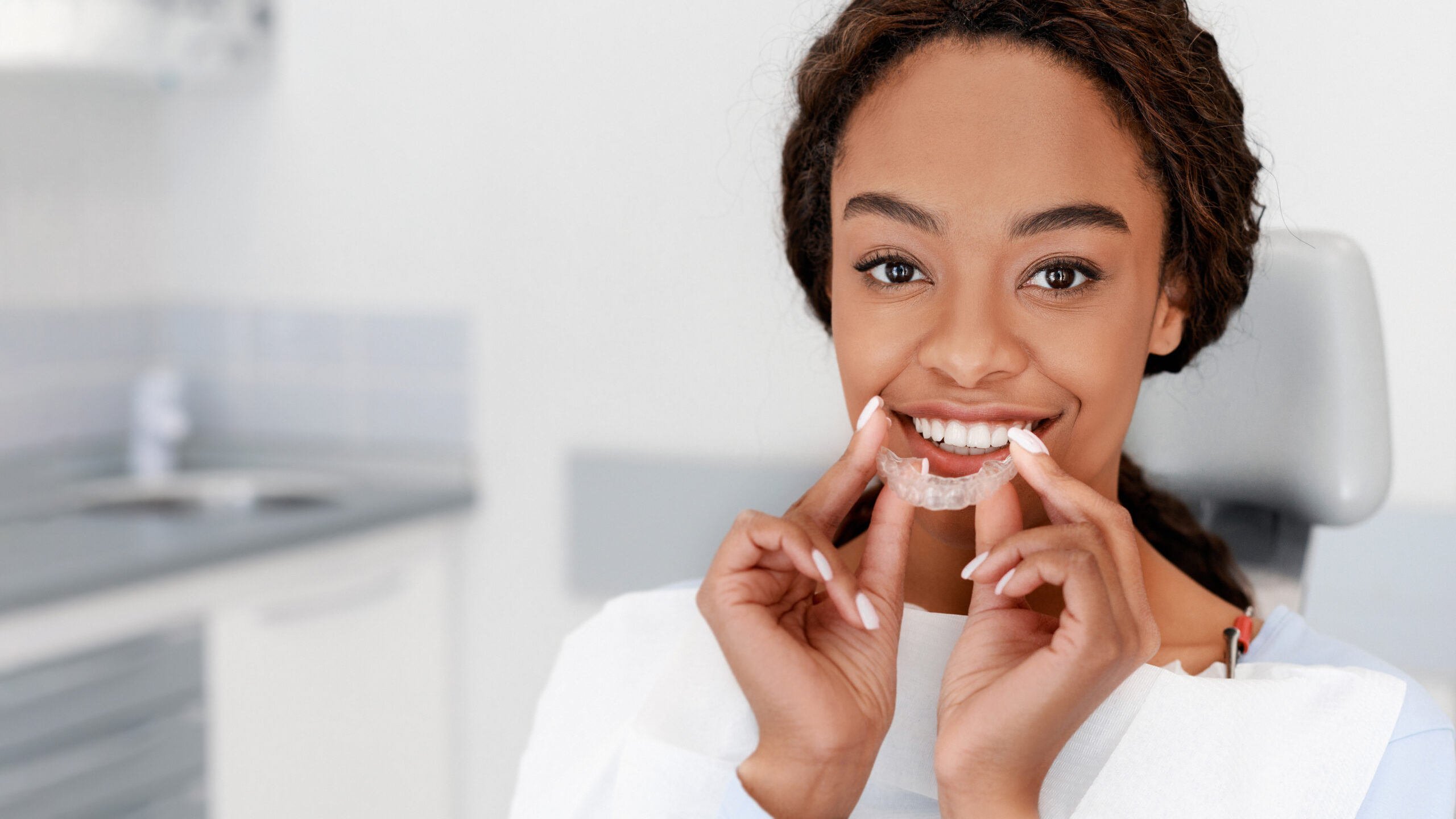 Smiling black girl holding invisible aligner, modern teeth trainer