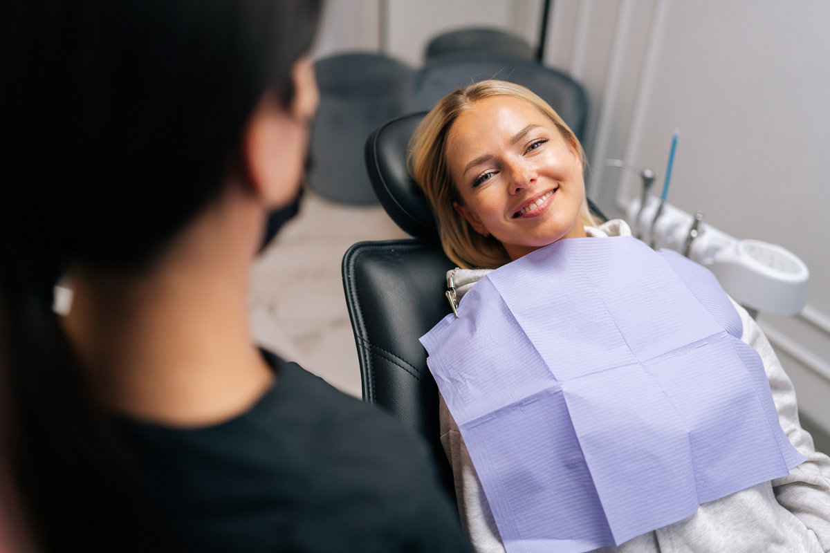 Close up front view of happy young woman patient with dental problem talking with unrecognizable dental doctor during checkup and consultation
